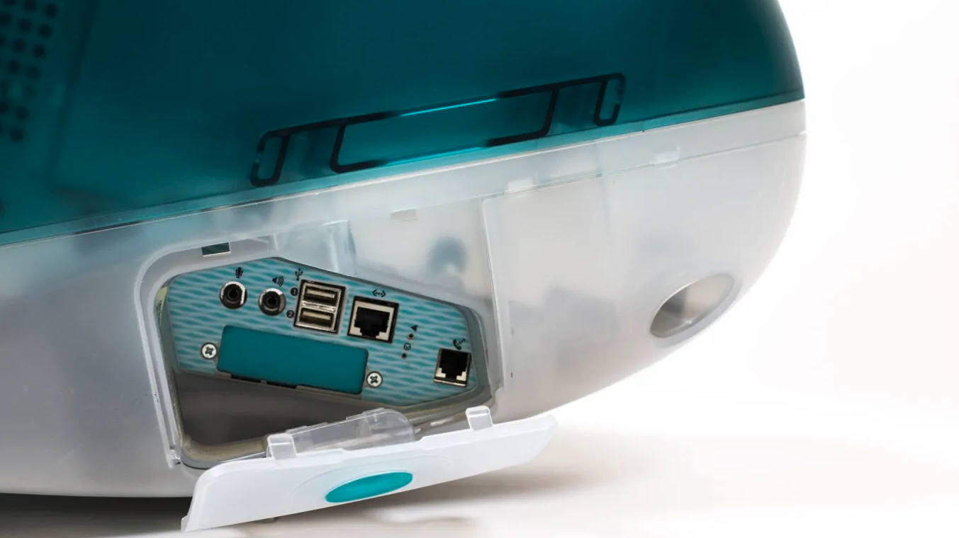 Close-up of the back of an Apple iMac G3, its translucent teal shell revealing ports and internal shielding.