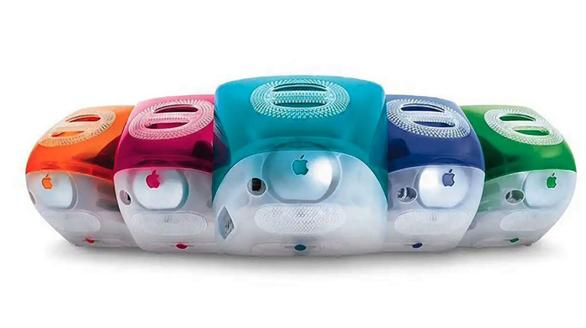 Five Apple iMac G3 computers side by side in orange, pink, teal, blue and green translucent casings.
